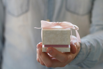 Man hand holding  ring in the white gift box with pink bow 