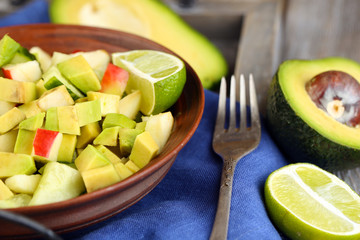 Salad with apple and avocado in bowl on tray on table close up