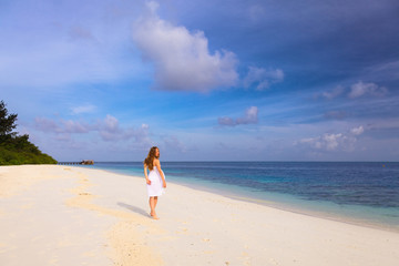 Fototapeta na wymiar Beautiful girl in a white dress walks on the Maldivian beach