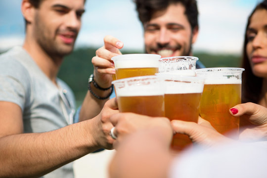 Vier Freunde mit Plastikbechern sto&szlig;en gemeisam an