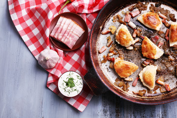 Fried dumplings with onion and bacon in frying pan,