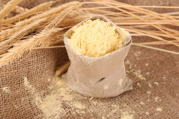 Flour in bag with wheat ears on burlap cloth, closeup