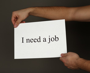Sheet of paper with inscription I need a job in male hands on dark background