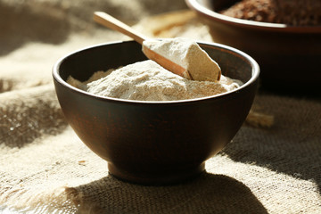 Flour in bowls with wooden scoop on burlap cloth background