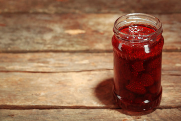 Jar of strawberry jam on wooden background