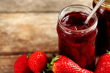 Jars of strawberry jam with berries on wooden background