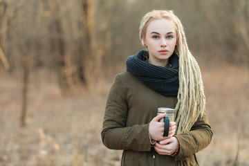 Young blonde woman with thermos cup cold season outdoors