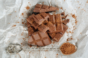 Pieces of chocolate with cocoa on parchment, closeup