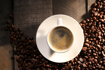 Cup of coffee with grains on wooden table, top view