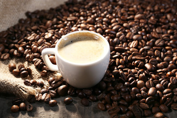 Cup of coffee and grains on wooden table with sackcloth,
