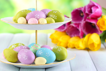 Easter eggs on vase and tulips on table on natural background