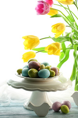 Easter eggs on vase and tulips on table on bright background