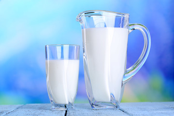 Pitcher and glass of milk on wooden table on natural background