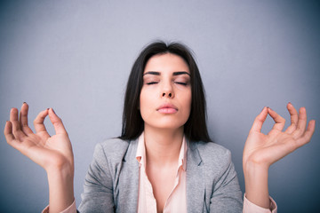 Young woman meditating over gray background