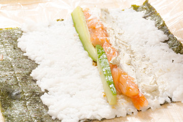 Hands cooking sushi with rice, salmon and nori