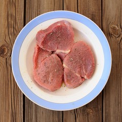 Raw veal in blue plate on wooden background