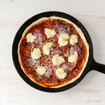 Raw round pizza with salami, onion, mozarella in cast iron skill