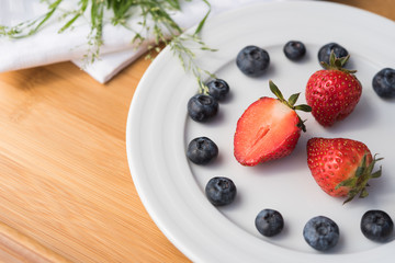 Plate with berries and bouquet of grass on white towel