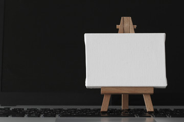 blank canvas and wooden easel on laptop computer as concept