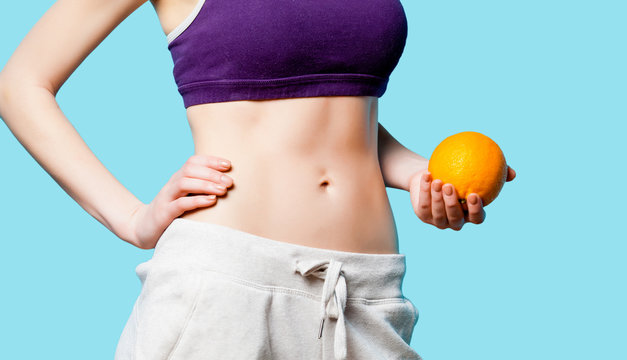 Woman showing her abs with orange after weight loss