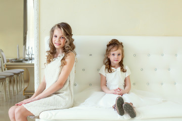 Smart girls posing at camera while sitting on sofa
