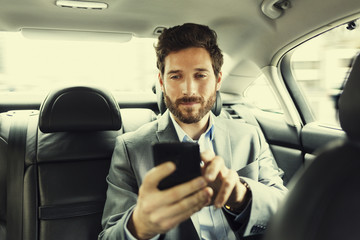 Hipster man in car. Typing text message on mobile phone