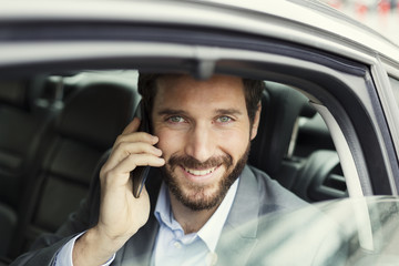Cheerful business man on mobile phone in rear of the car