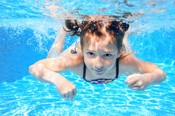 Happy girl swims in pool underwater, active kid swimming