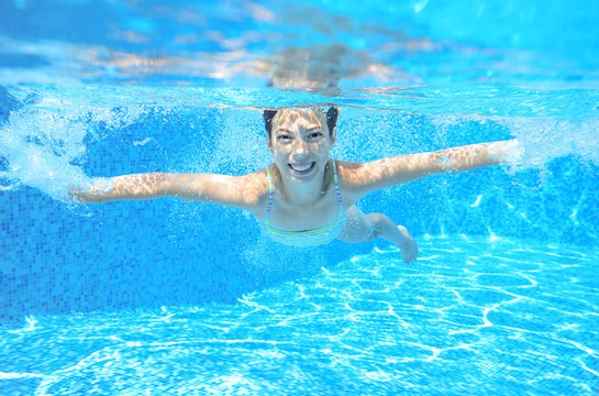 Happy girl swims in pool underwater, active kid swimming