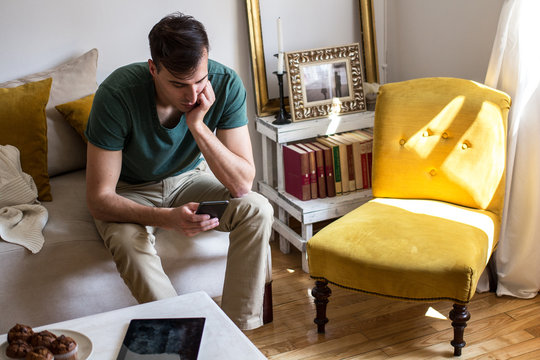 Man Sitting On Couch And Using Phone At Home In The Living Room