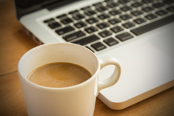 Hot latte coffee cup and laptop on wood background and texture.