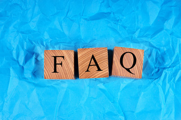 Cubes with an inscription FAQ on crumpled blue paper. Top view.