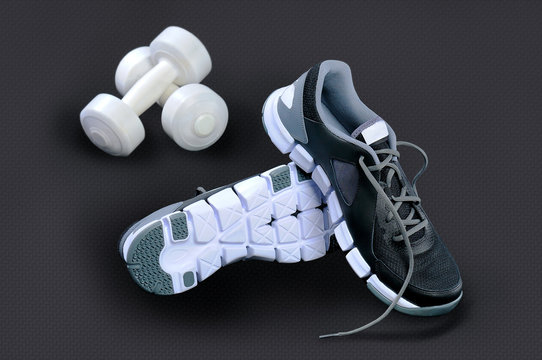 Black-and-white sneakers and white dumbbells against a dark back
