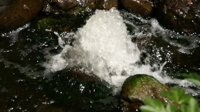 Slow motion view of spring water between rocks and sunshine.