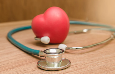 Red heart and stethoscope on wooden background.