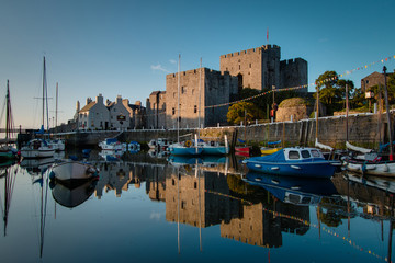 Sunrise at Castletown Harbor in the Isle of Man with Castle Rushen and boats reflecting in the...