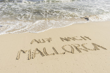 Text AUF NACH MALLORCA in Sand gezeichnet mit Wellen