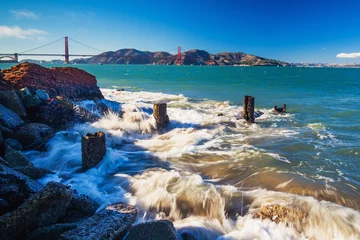Papier Peint photo San Francisco Surf splashes over rocks with the view of Golden Gate Bridge
