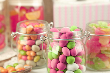 Multicolor candies in glass jars on wooden background