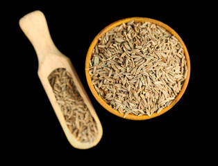 Cumin in wooden bowl, isolated on black