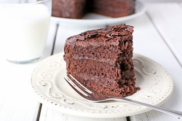 Sliced tasty chocolate cake in plate on wooden table, closeup