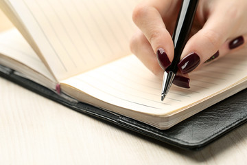 Female hand writing in diary by pen on wooden table background