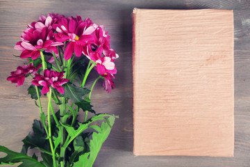 Bouquet of flowers with book on wooden table, top view