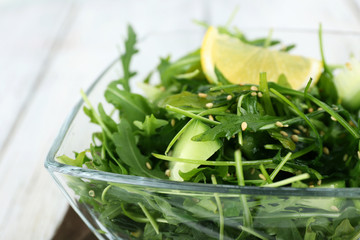Glass bowl of green salad on wooden table, closeup