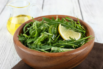 Bowl of green salad and sliced lemon on wooden table, closeup