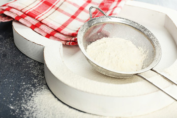 Sifting flour through sieve on wooden table, closeup