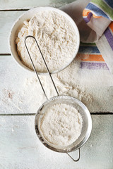 Sifting flour through sieve on wooden table, top view