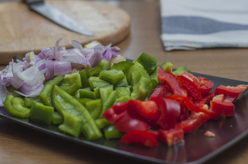 Sliced green and red peppers and onion on a wooden table