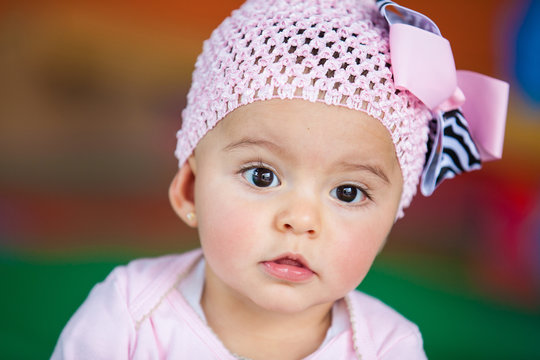 Rostro de una hermosa bebita de seis meses vestida de rosa en actitud pensativa con un fondo colorido