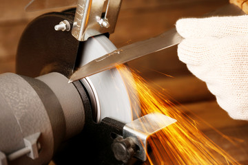 Knife sharpener and hand with blade on wooden table, closeup
